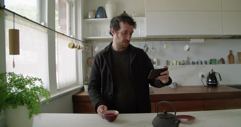 A man drinking tea and talking on his smartphone