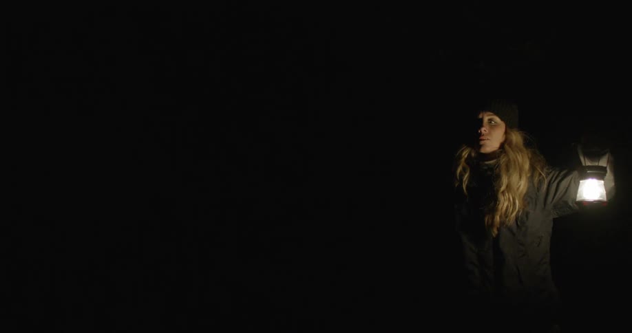 A blonde person holds a lantern in a dark area