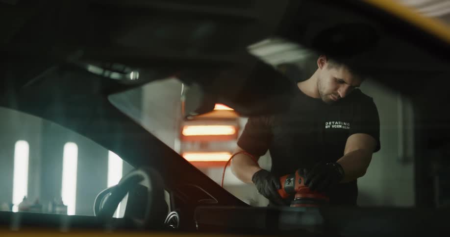 A man uses a buffering machine on the surface of a hood of a car in a garage
