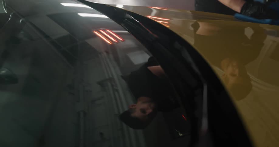 A man uses a cloth to buff the paint on a car inside a clean garage