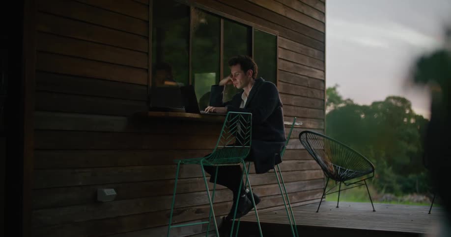 A man sitting outdoors typing on a laptop