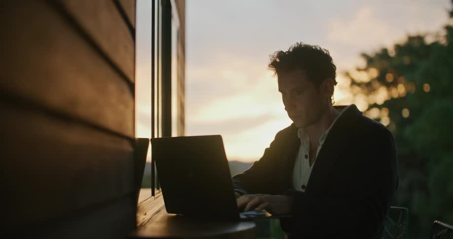 A man using a laptop with trees the sky and clouds in the background