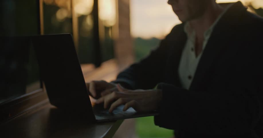 A man using a laptop with trees the sky and clouds in the background