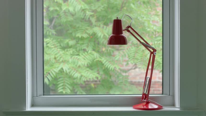 A red lamp sits on a window ledge next to lush green bushes