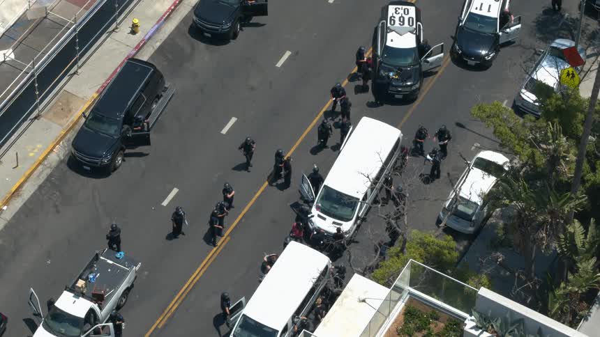 A suspect in hand cuffs is escorted down a street while surrounded by police