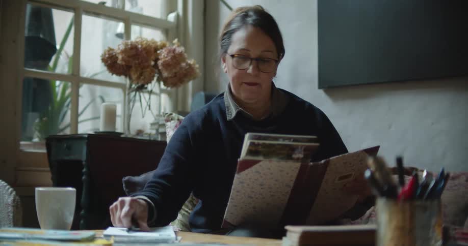 Woman flips through a photo album and stops to write something in a notebook