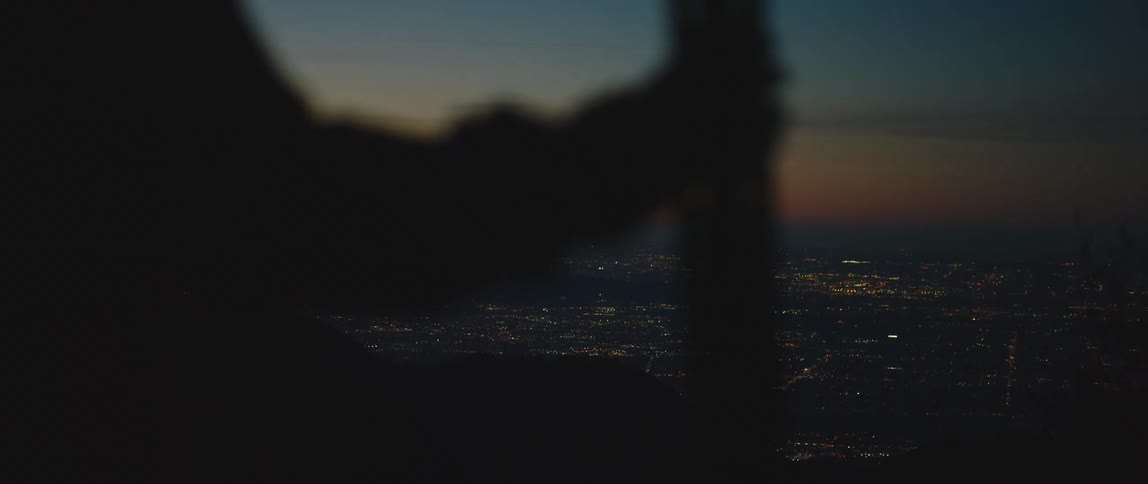 A person stands overlooking a sprawling city at night as the sun is slightly below the horizon