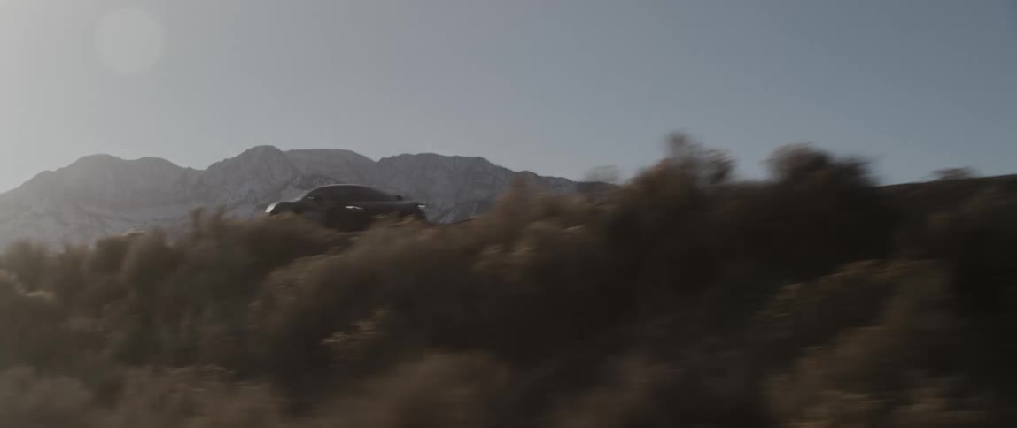 A sports car drives down a road next to a hill