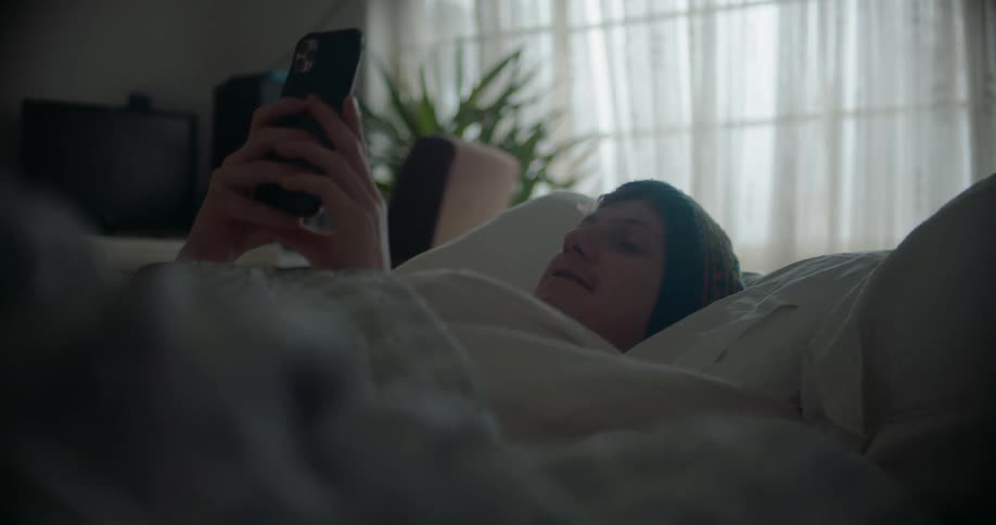 A man uses his smartphone while relaxing in bed during the day