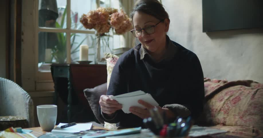 Woman sitting on a couch at home looking at photographs over a coffee table