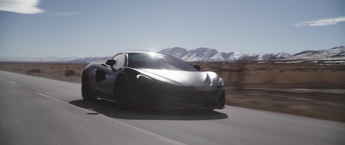 A black sports car speeds down a rural road near snow capped mountains