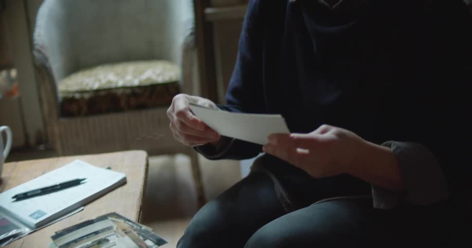 A woman sits on her couch and goes through a stack of printed photographs