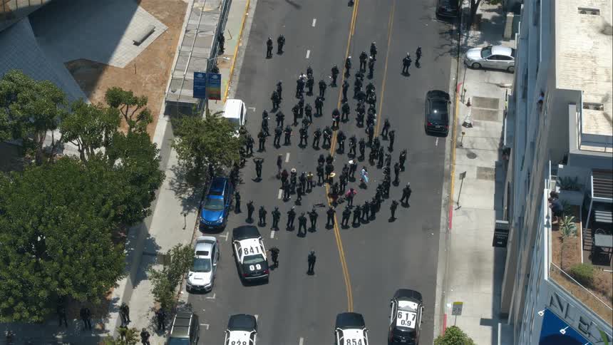 Group of police officers form a circle on the street with police cars parked nearby