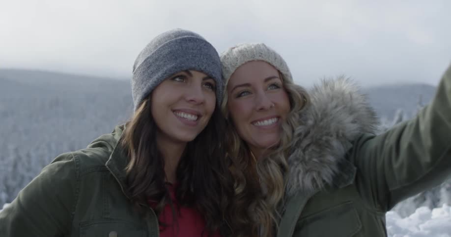 Two women take pictures on a snowy mountain