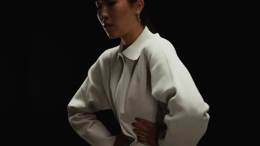 Woman with hoop earrings a white blouse stands hands on waist on the dark background