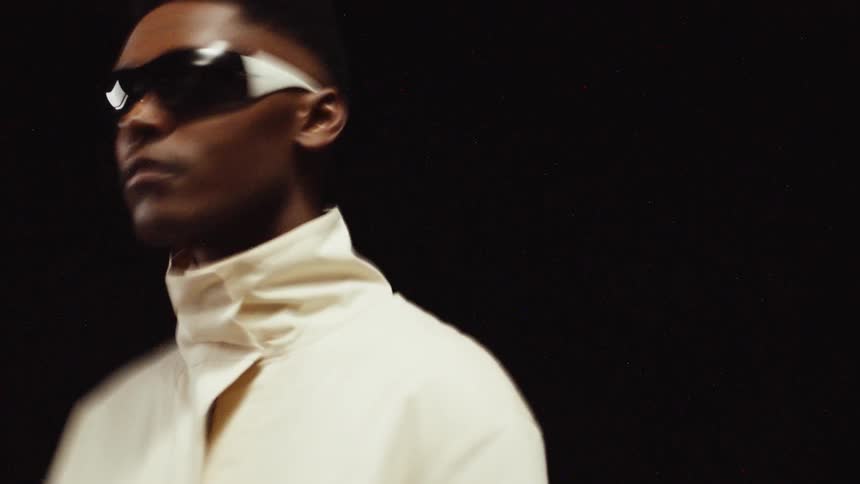 Young man wearing sunglasses and a white jacket models for the camera