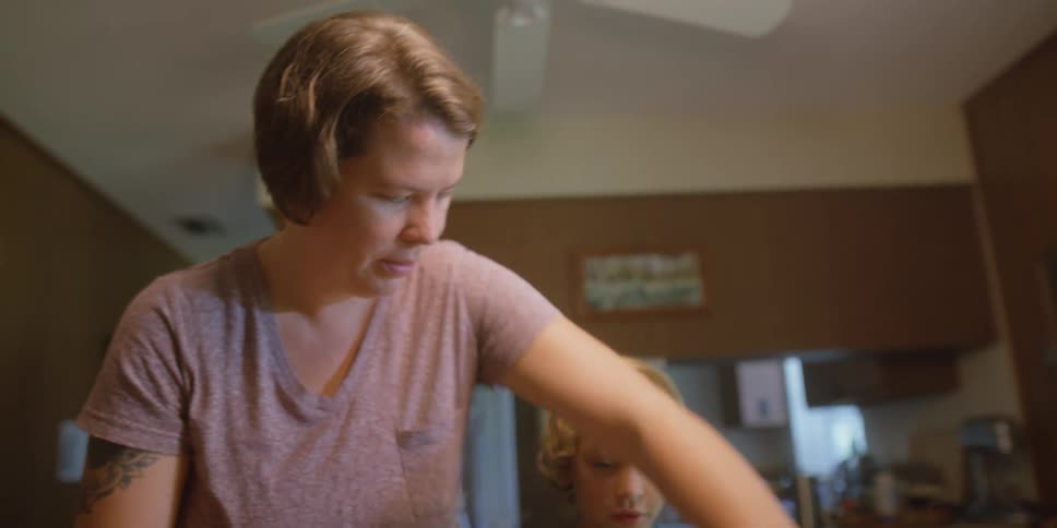 A woman helps a young boy making a sandwich in their home kitchen