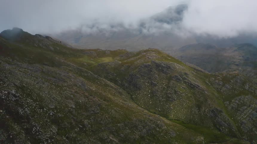 Grass covered mountains with peaks high in a cloud filled sky