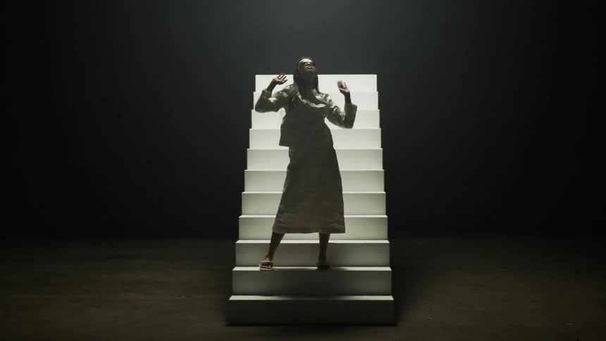 A model posing on a rotating set of stairs raises her arms above her head