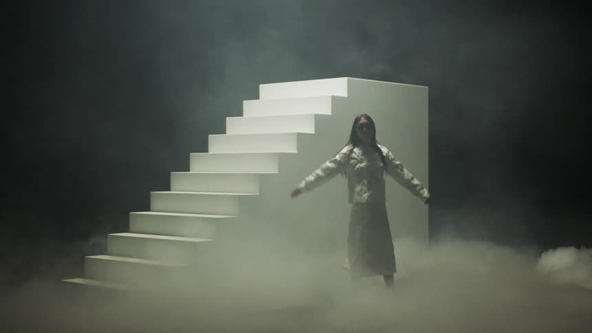Woman spins and poses near rotating staircase on foggy stage