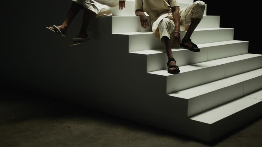Two people with slippers in a room sitting on a staircase with a wall in the background