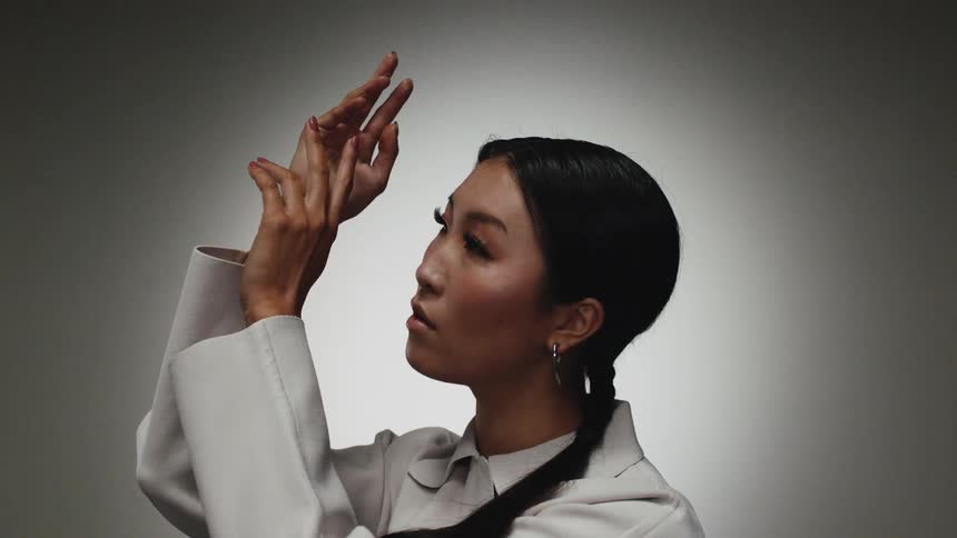 A woman is standing next to a wall and wearing a coat