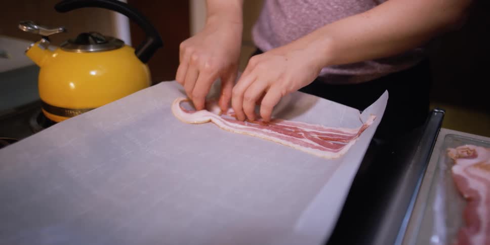 A woman places strips of bacon on a pan with parchment paper