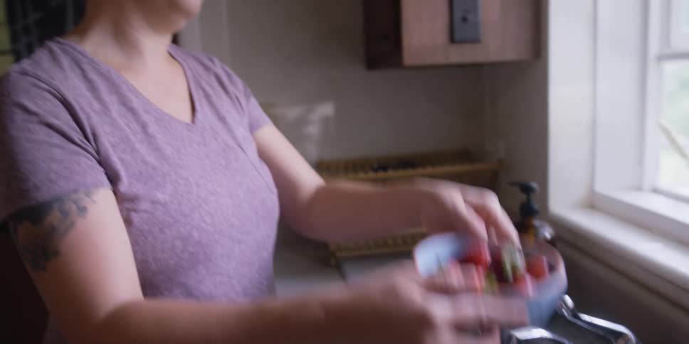 Woman with a purple shirt washes a bowl of strawberries in the kitchen