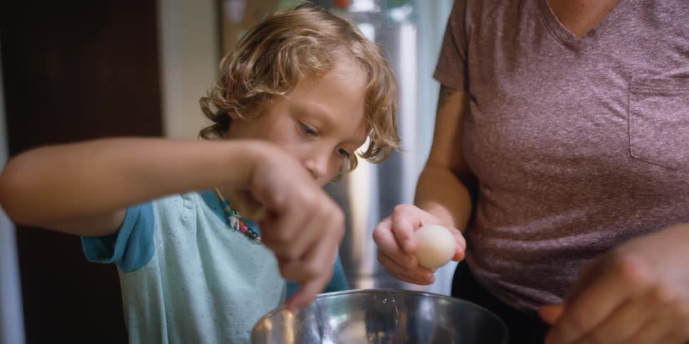 A boy and a woman in a kitchen mixing eggs in a bowl