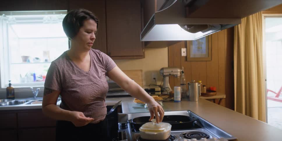 A woman stands in her kitchen as she works on a dish of food that she is cooking
