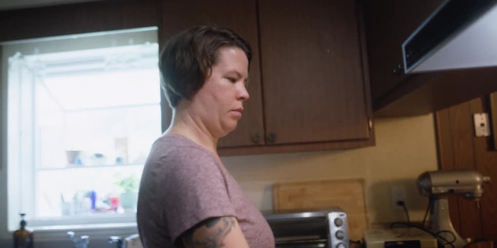 A woman is standing at a stove stirring food in a pan
