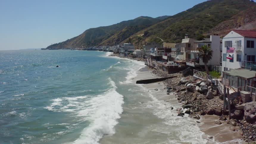 Waves curl and break along a beach lined with homes and hills