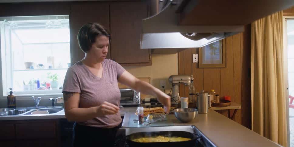 A woman adds seasoning to a pan of eggs cooking on the stove