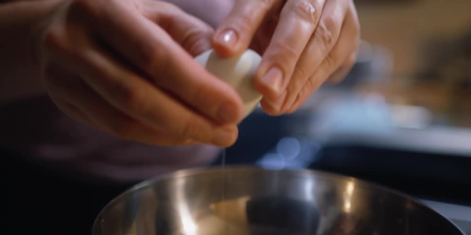 A person in a kitchen cracking open an egg and putting it in a bowl with a wall in the background