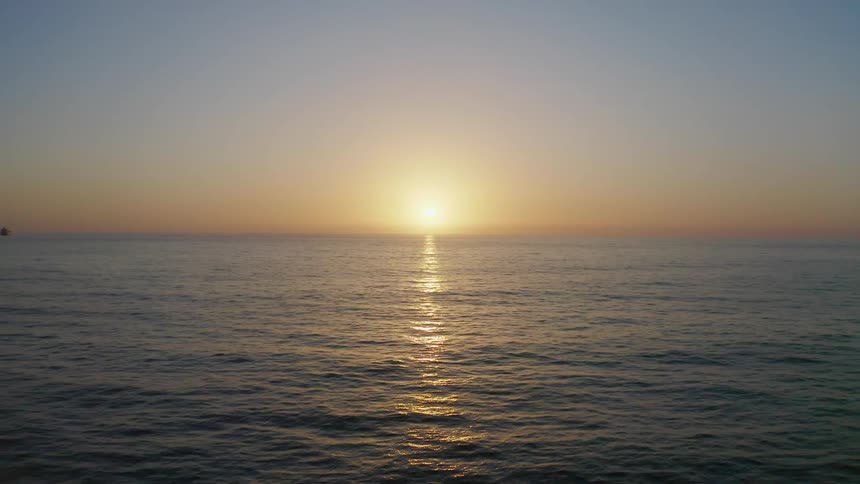 The sun sits low on the ocean horizon on a clear evening