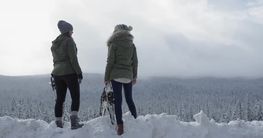 Two women stand overlooking a snowy ridge and high-five