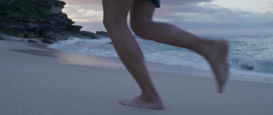 Man runs along the white sand beach next to the ocean at sunset