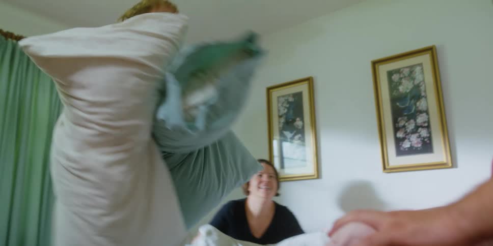 Parents pillow fighting their son over the bed in the bedroom at home