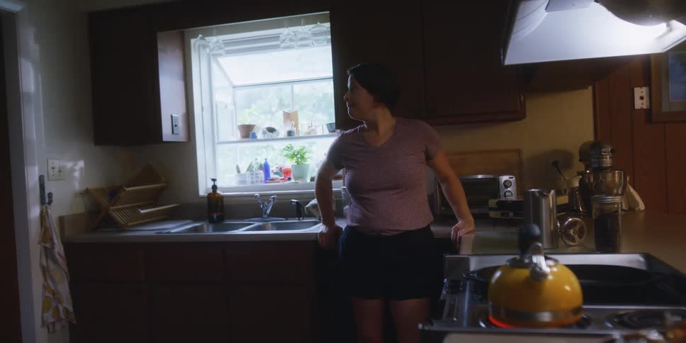 A woman watches a kettle set on a hot stove while standing in a kitchen