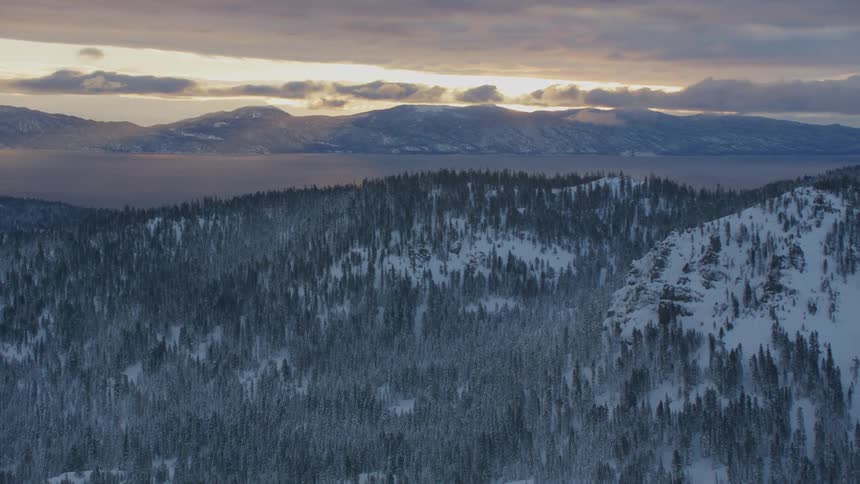 A snowy mountain range covered in forest on a cloudy evening