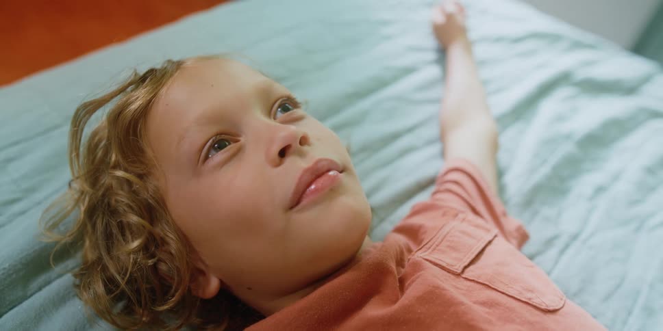 A young boy smiles while lying on a bed with his arms spread wide