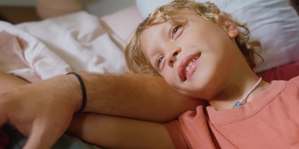 A boy rests his head on his fathers forearm while lying down