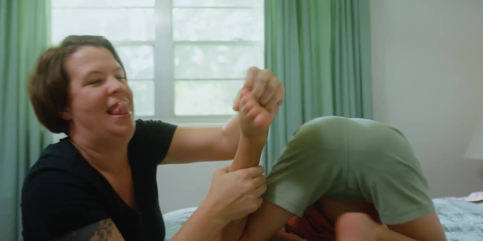 Mother tickles childs feet as child rolls around on bed kicking