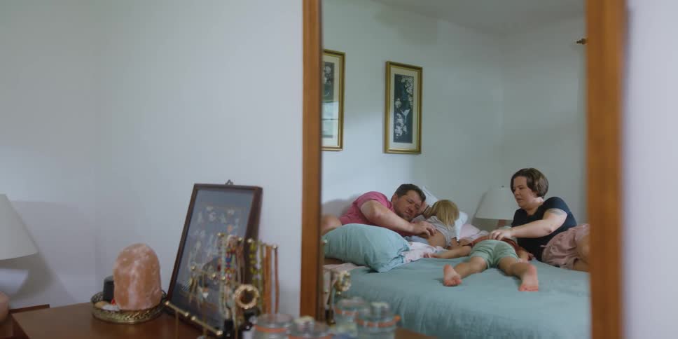 Looking through a dresser mirror a family lays on a bed together