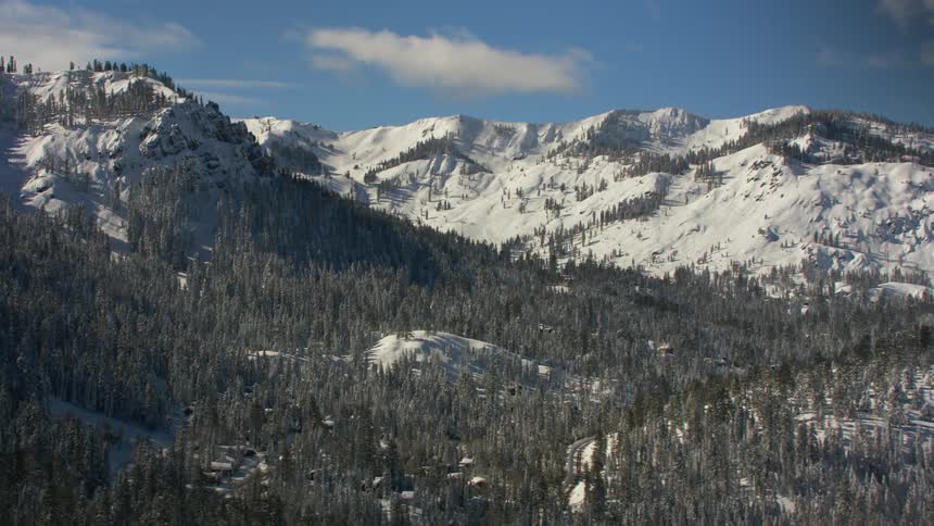 Snow covered mountains and forests with a few scattered clouds in a blue sky