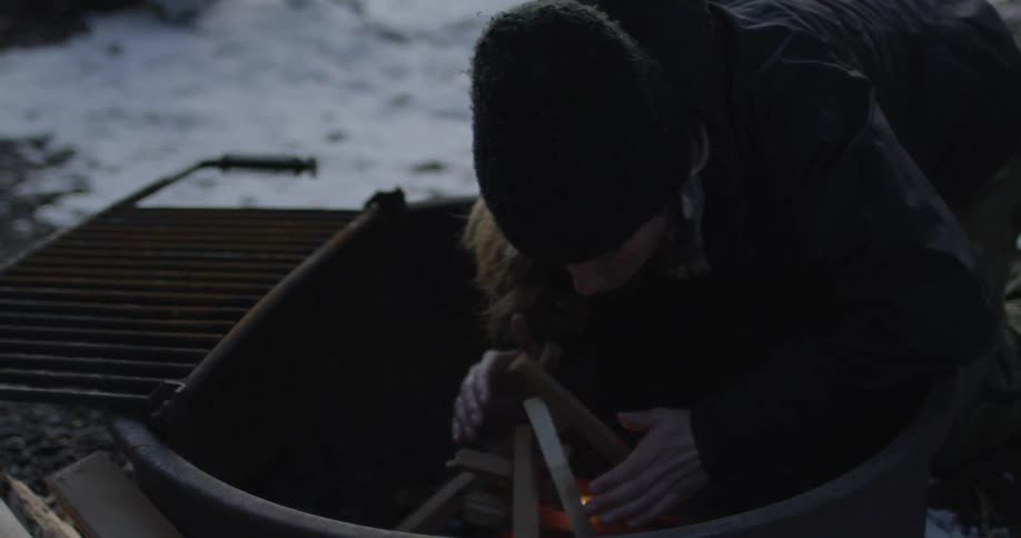 A woman crouches down to blow on a fire