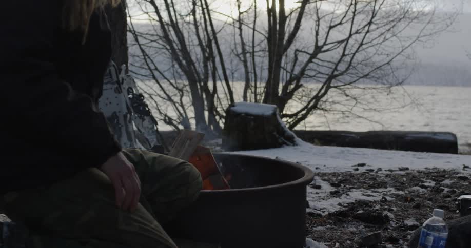 Person sitting next to a fire in a barrel in the winter