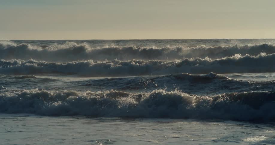 Waves closely follow waves all of them crashing onto beach on overcast day