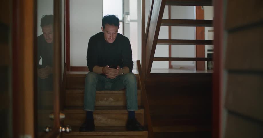 A man is sitting on the landing of a staircase looking at his cellphone