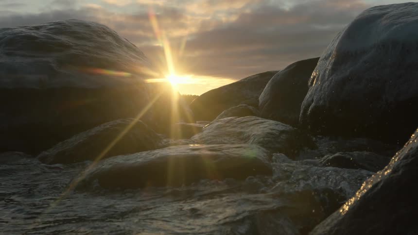 Waves crash against smooth rocks at sunset